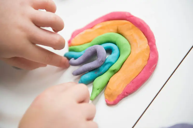 Kinderhände formen einen Regenbogen aus bunter Knete